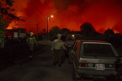 El fuego cerca la localidad de Bustelo de Lor. Un vecino y un bombero forestal caminan por una de las calles de Bustelo de Lor en la larga noche de los incendios del lunes