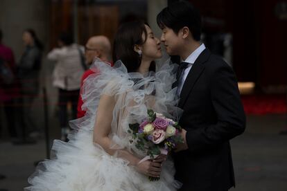 Una pareja de novios coreanos se hacen fotos con un ramo de rosas frente a la casa Batllo. 