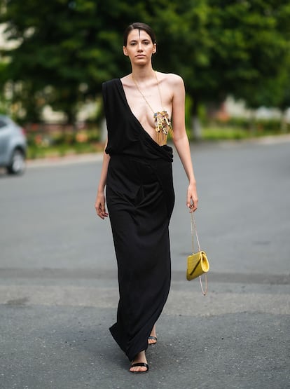 Una invitada a la Feeric Fashion Week, en Rumanía, con un vestido negro asimétrico y un collar dorado que le cubre el pecho.