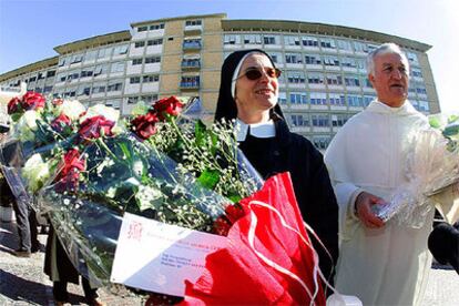 Una monja y un sacerdote llegan con flores al policlínico donde está ingresado el Papa.