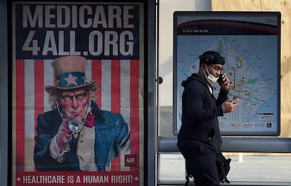 Un hombre mira el móvil al lado de un cartel de Medicare (seguro de salud para mayores en EE UU) en Washington DC.