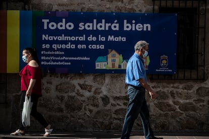 Dos vecinos de Navalmoral de la Mata pasan junto a un cartel que pide a los vecinos quedarse en casa por el coronavirus.