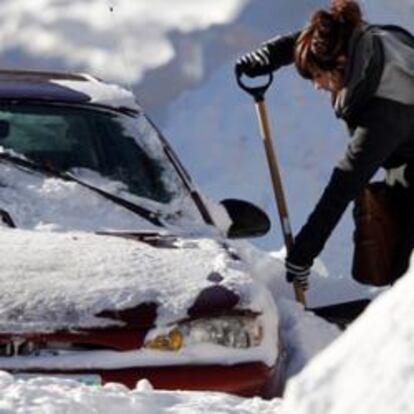 Un mujer trata de limpiar de nieve su vehículo en Minneapolis