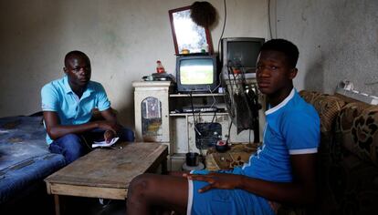 Abdoulaye Dosso (izq.) regresó de Libia voluntariamente. Se sienta junto a un pariente en su casa en Abiyán.
