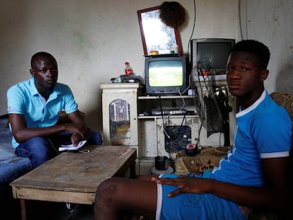 Abdoulaye Dosso (izq.) regresó de Libia voluntariamente. Se sienta junto a un pariente en su casa en Abiyán.