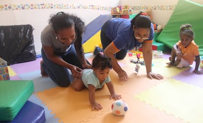 Una madre juega con su hija pequeña ante la mirada de la mayor y con la ayuda de una experta, en un centro de atención a la primera infancia en Boca Chica.