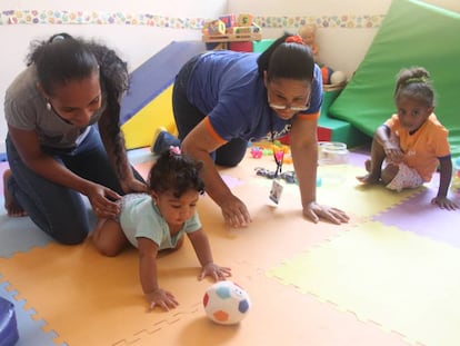 Una madre juega con su hija pequeña ante la mirada de la mayor y con la ayuda de una experta, en un centro de atención a la primera infancia en Boca Chica.