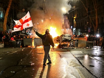 Un hombre alza la bandera de Georgia ante una barricada levantada con un coche destruido frente al Parlamento en la noche del 8 al 9 de marzo.