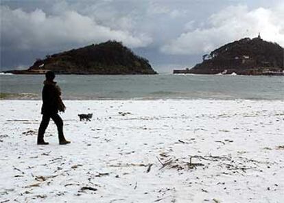 Una mujer camina con su perro sobre la nieve que cubría ayer la playa de Ondarreta, de San Sebastián.