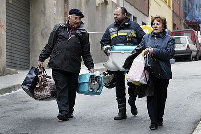 Afectados por el hundimiento del Carmel salen de recoger enseres de sus domicilios acompañados por un bomberos.