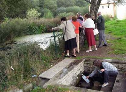 Una mujer llena una botella en Codesido mientras un grupo de visitantes contemplan la charca.