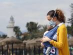 Una mujer protegida con una mascarilla da un paseo con su bebé en la playa de La Malagueta.