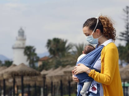 Una mujer protegida con una mascarilla da un paseo con su bebé en la playa de La Malagueta.