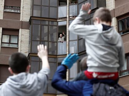 Duas crianças acenam para seu avô, que está na janela de sua casa em Pamplona.