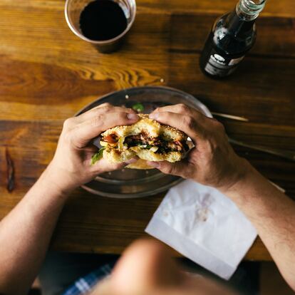 An aerial view of a man eating a burger and drinking cola in a restaurant.