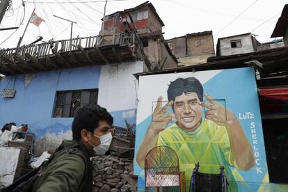 Daniel Manrique camina junto al mural que ha pintado en el Cerro San Cristóbal de Lutz Sherlock, un joven de 20 años fallecido por cáncer de estómago en plena pandemia, en Lima (Perú). Detrás de los fallecidos durante la cuarentena hay historias y rostros que en Perú, el quinto país del mundo con más contagios de covid-19, han comenzado a emerger en forma de murales gracias a un artista empeñado en mantener vivo el recuerdo de sus vecinos para que no caigan en el olvido.