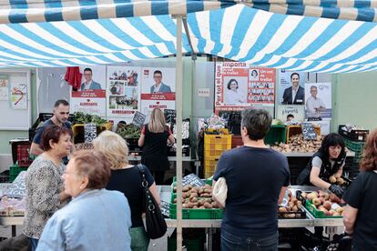 Vecinos de Almussafes esperan su turno en un puesto de frutas y verduras del mercadillo, situado junto a propaganda electoral, este pasado martes.