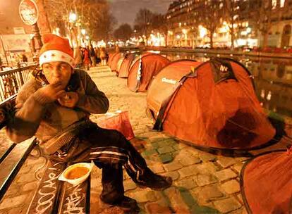 Una persona sin domicilio fijo cena, el pasado lunes en París, ante las tiendas instaladas a la orilla del Sena.