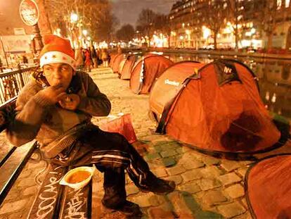 Una persona sin domicilio fijo cena, el pasado lunes en París, ante las tiendas instaladas a la orilla del Sena.