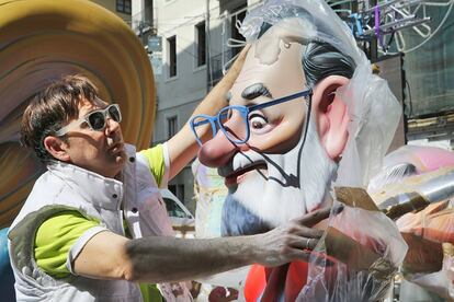 Un hombre retira el plástico que cubre un ninot de Mariano Rajoy con gafas azules.