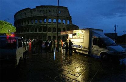 Un grupo de romanos se cobija al amanecer en un puesto de comidad callejera, único punto con luz frente al Coliseo.