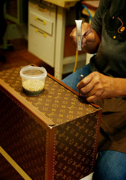 An artisan places rivets on the canvas of a trunk.