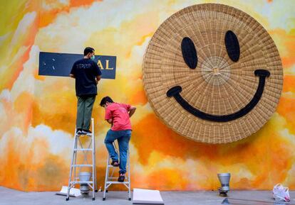 Dos trabajadores instalan un letrero junto a un emoji sonriente en el exterior de un centro comercial en Bangkok (Tailandia). Las autoridades sanitarias de Tailandia anunciaron este viernes que recortarán a partir de abril a 7 días la cuarentena obligatoria para los viajeros que procedan del extranjero siempre y cuando ya hayan sido vacunados contra la covid-19.