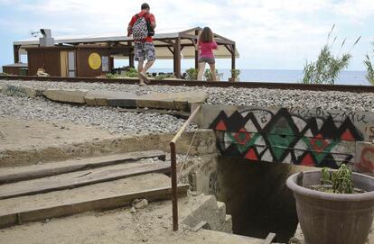 Dos personas cruzan la v&iacute;a del tren a pie ignorando un paso bajo nivel en Sant Pol de Mar.