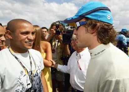 Alonso ha contado con la visita inesperada del madridista Roberto Carlos (izqda.) antes de comenzar el Gran Premio.