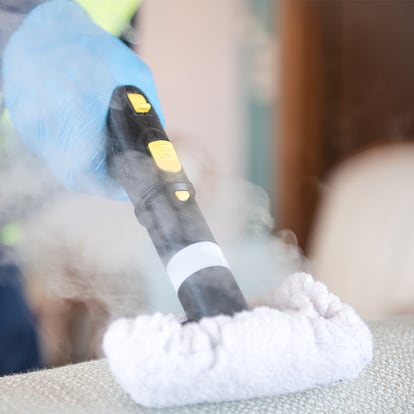 Una persona limpiando un sofá con una vaporeta de mano.