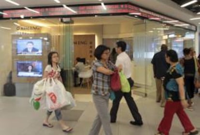 Clientes de un centro comercial pasan junto a una pantalla que muestra resultados de la Bolsa de Singapur. EFE/Archivo