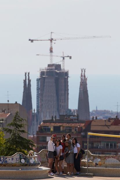 Varias personas se fotografían en el banco del Park Güell. Al fondo la Sagrada Familia.