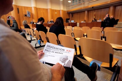 Una de las personas del público del juicio por Meirás sostiene un cartel de la concentración convocada a las puertas de los juzgados para reclamar la devolución. La asistencia de público a la vista se ha restringido por la pandemia.