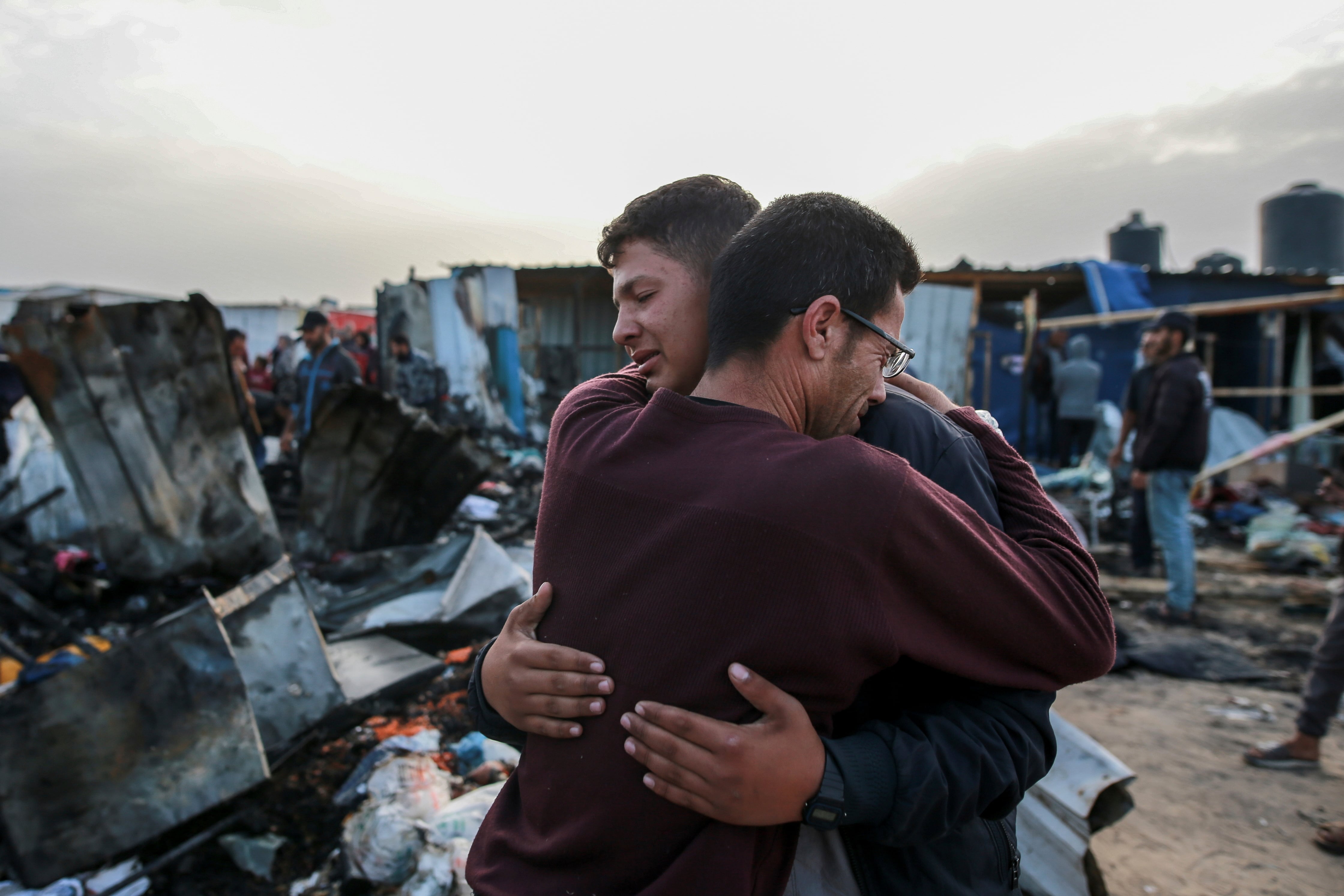 Dos hombre se abrazan junto a los restos de las infraviviendas atacadas por el ejército israelí en un campo de desplazados en Rafah, este lunes. 