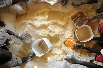 2005, Saraf Omra, Darfur norte, Sudán. Hacen falta muchas manos para facilitar el acceso a alimentos nutritivos. El proceso que lleva los alimentos hasta las poblaciones necesitadas es largo y complejo. La entrega final la suelen hacer las ONG, muchas de ellas locales y siempre con la ayuda de personal contratado en los lugares donde se realizan las distribuciones. La cesta de alimentos que distribuye el PMA se suele componer de cereales, legumbres, aceite, CSB y sal. En la imagen, distribución de harina enriquecida de maíz y soja, CSB en la jerga humanitaria. La luz que se colaba por los agujeros del techo de la carpa parecía jugar con las ocupadas manos.