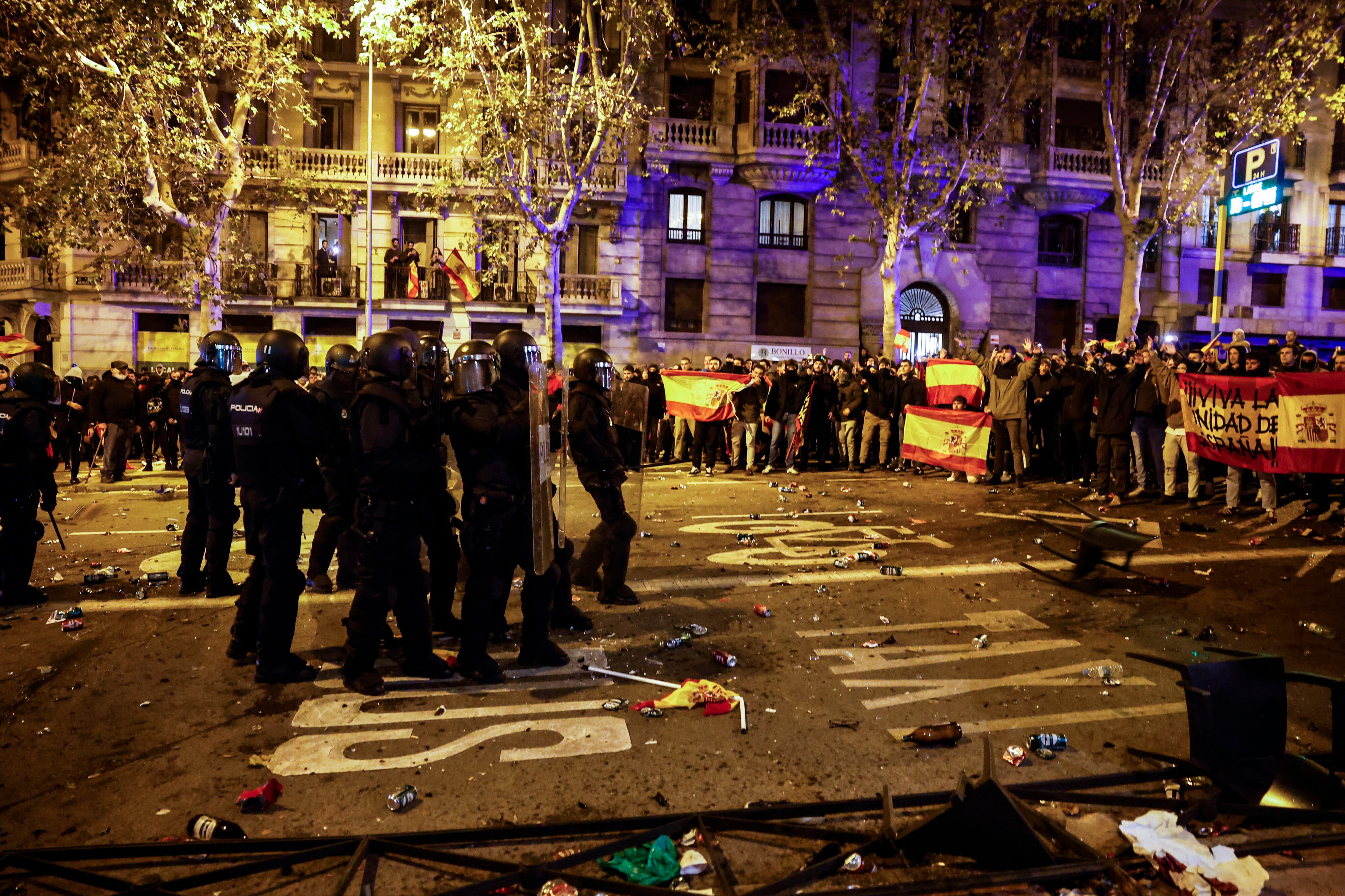 Agentes se agrupan al tiempo que manifestantes lanzan objetos contra ellos. 