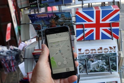 Un hombre utiliza la aplicación de Uber frente a una tienda de venta de postales turísticas en Londres.