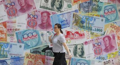 Una mujere camina en Hong Kong junto a un mural decorado con diferentes divisas
