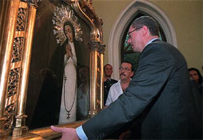 El alcalde, Alberto Ruiz-Gallardón, contempla el cuadro con la imagen de la Virgen de la Paloma, tras ser bajado del altar por los bomberos.