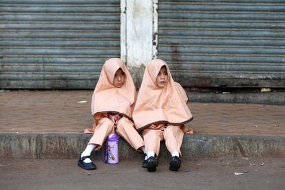 Dos niñas en uniforme se sientan en la acera mientras esperan al autobús escolar en Karachi (Pakistán)