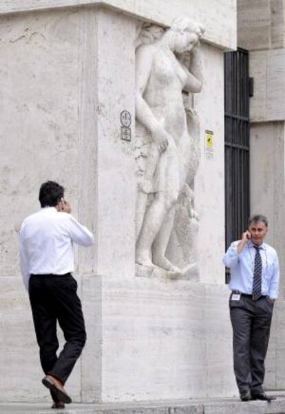 Dos consultores financieros hablan por teléfono móvil junto al edificio de la Bolsa en la plaza Affari de Milán (Italia). EFE/Archivo
