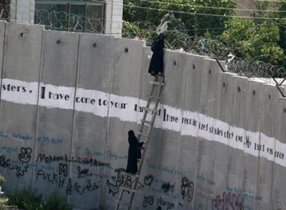 Dos mujeres se encaraman a una escalera cerca de la localidad de A Ram para poder seguir el rezo de la mezquita de Al-Aqsa, en Jerusalén.