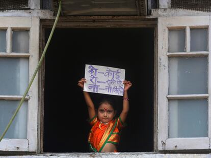 Una niña en Mumbai, India, muestra desde la ventana un cartel para pedir que nadie salga a la calle