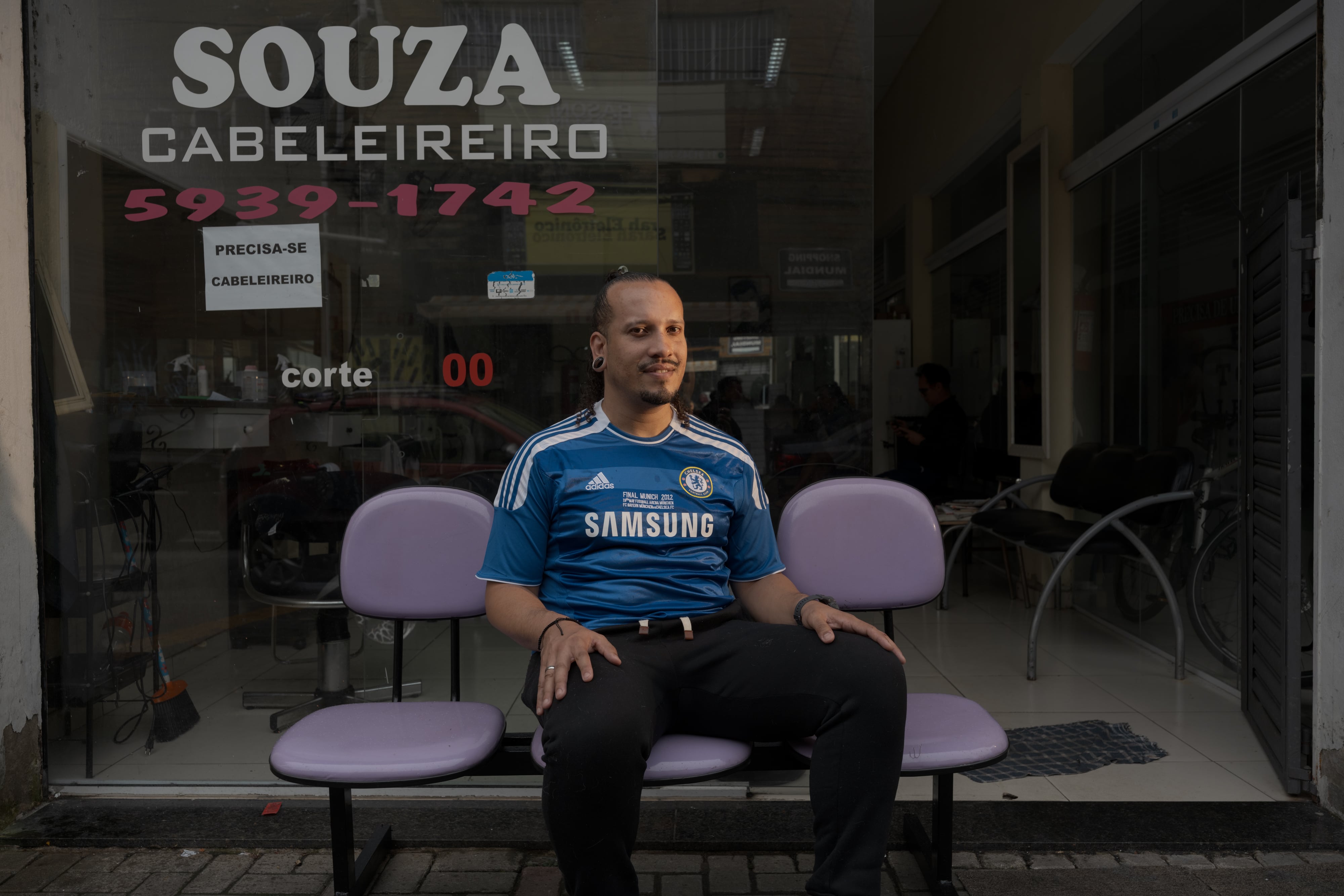 Robson Souza, de 37 años, en una de las sillas para clientes frente a su peluquería en Vila São José, en São Paulo.