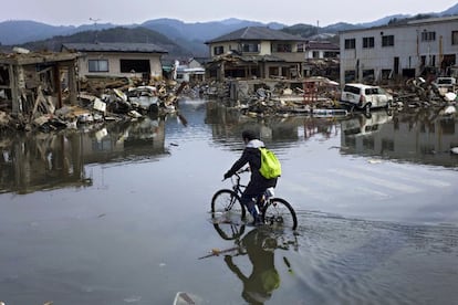 Un hombre conduce una bicicleta por una calle inundada en el devastado Puerto de la ciudad de Kesennuma, Miyagi.