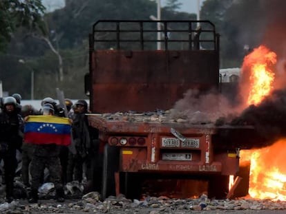 Fuerzas de seguridad venezolanas muestran una bandera junto a camión quemado con ayuda humanitaria. 