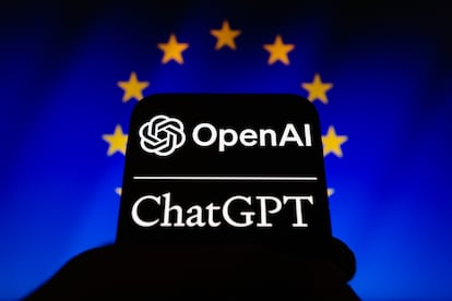 Los logos de OpenAI y ChatGPT en un teléfono móvil frente a un cartel con la bandera de la UE.