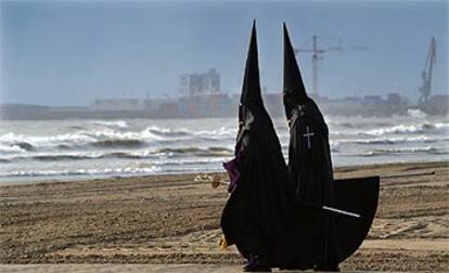 Dos cofrades de la hermandad del Santísimo Cristo del Salvador pasean por la playa durante la procesión realizada a primera hora de la mañana en Valencia para rezar en la orilla por los difuntos del mar y las víctimas del 11-M.