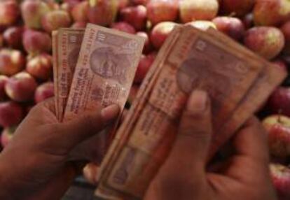 Un vendedor indio cuenta varios billetes en un puesto instalado en una carretera de Bombay, India, hoy, lunes 19 de agosto de 2013.