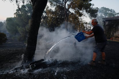 José Pérez intenta contener las llamas lanzando agua en el jardín de su vivienda, mientras un incendio forestal avanza por las afueras de Valmojado (Toledo), este jueves.